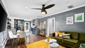 A modern living room with a green sofa, a dining area with white chairs, and a kitchen with dark cabinets. - Relaxing Oasis - Walk to Lake Austin, Pet Friendly
 (Austin)