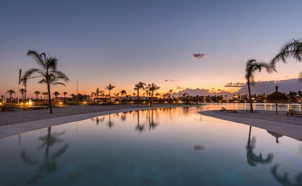 A tranquil pool area with palm trees and a sunset view.