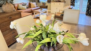 Een woonkamer met een bank, salontafel en een vaas witte bloemen.