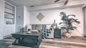 A living room with a sofa, coffee table, and a potted plant.
