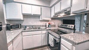 A modern kitchen with white cabinets, a built-in microwave, a stove, and a sink.
