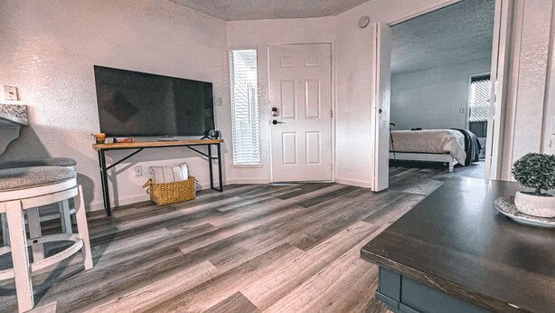 A room with a wooden floor, a desk with a chair, a television, and a bed.