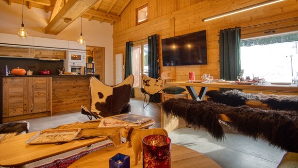 Un interior rústico de madera con cocina, zona de estar y un televisor grande.
