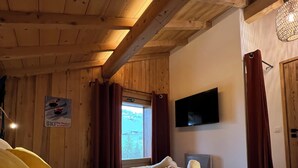 Un dormitorio tipo cabaña de madera con cama, televisor y ventana con cortinas.