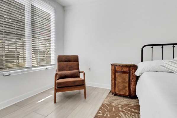 Un dormitorio con cama, una silla, una mesita de noche y una ventana con persianas.