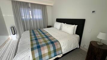 A hotel room with a bed, curtains, a bedside table, and a lamp.
