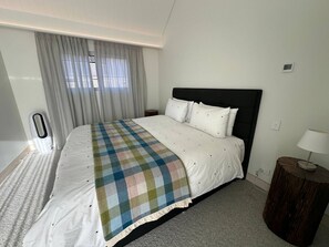 Hotellihuone, jossa on suuri sänky, yöpöytä, lamppu ja ikkuna, jossa on verhot.