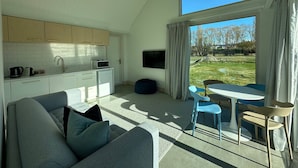 Un salon moderne comprenant un canapé, une table à manger avec des chaises, un coin cuisine et une grande fenêtre donnant sur l’extérieur.