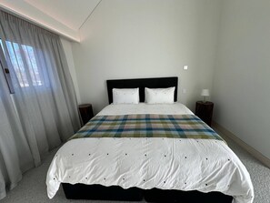 A neatly made bed with a plaid blanket, two bedside tables with lamps, and a window with curtains. - Lyford Luxury Lodge, Guest Wing (Twizel)