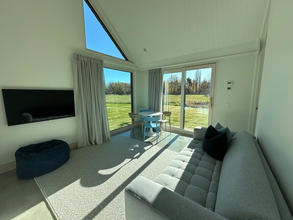 A modern living room with a large sofa, a flat-screen TV, and a dining area with a table and chairs. - Lyford Luxury Lodge, Guest Wing (Twizel)