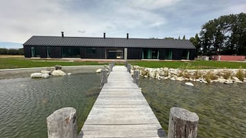 A wooden dock leading to a modern building with a dark roof, surrounded by water and rocks.