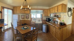 Una cocina con armarios de madera, una mesa de comedor, sillas, un refrigerador, un microondas y un fregadero.
