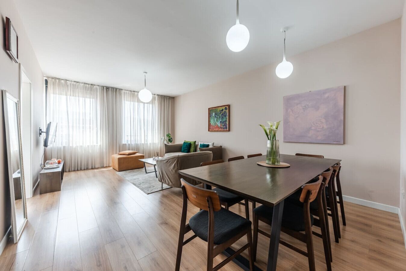 A modern living room with a dining area, wooden flooring, and a large painting on the wall.