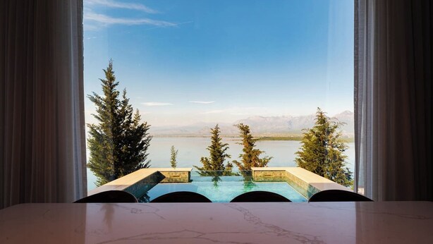 Vista desde una habitación con una mesa de mármol, con vista a un lago y montañas.