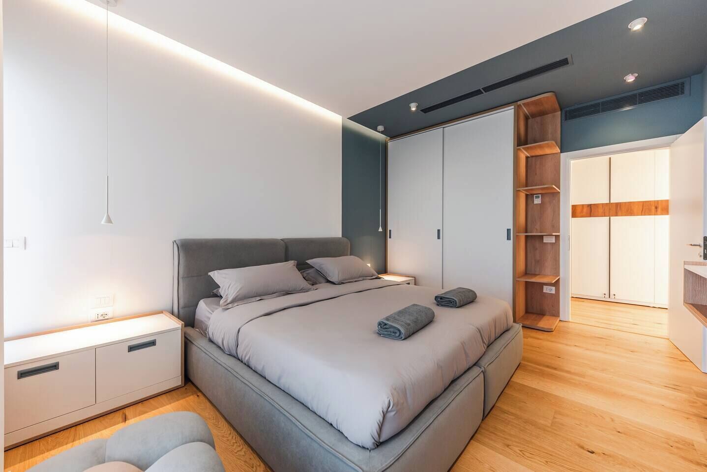 A modern bedroom with a large bed, built-in wardrobe, and a small seating area.