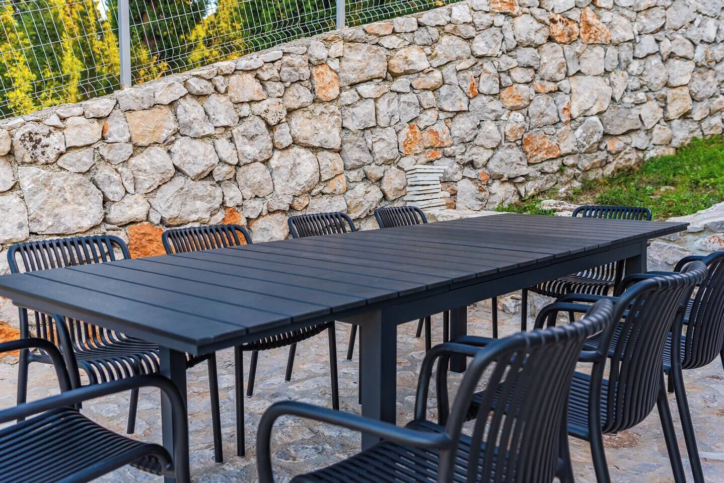 A stone wall with a metal fence behind it, a black metal table with chairs, and a stone floor.