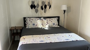 A bedroom with a bed, a bedside table, a lamp, and a wall-mounted decoration. - Quaint Cabin #3 - Pymatuning Lake (Jamestown)
