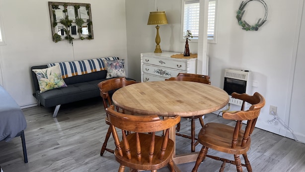 A dining area with a round wooden table and four chairs, a sofa with floral cushions, a white dresser, and a decorative mirror. - Quaint Cabin #3 - Pymatuning Lake (Jamestown)