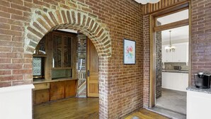 A room with a brick wall, wooden flooring, a staircase, and a kitchen visible through an open doorway. - Woodruff Manor 11 Bedroom Estate - 20+ guests (Indianapolis)