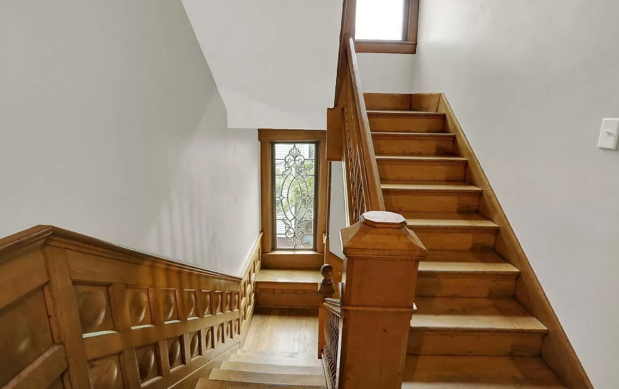 A wooden staircase with a handrail, a window with a decorative iron grille, and a light switch on the wall.