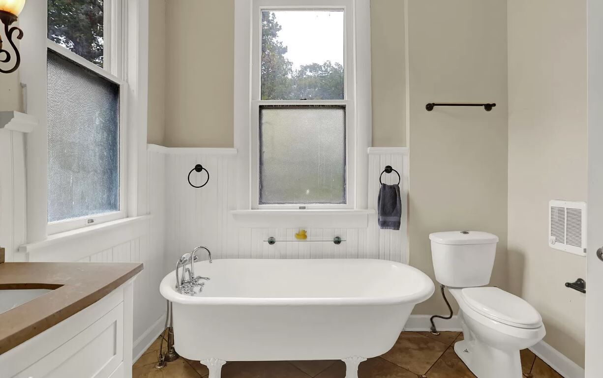 Un baño con bañera independiente, inodoro, ventana y perchero.