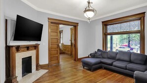 A living room with a flat-screen TV, a fireplace, a sectional sofa, and a large window with a view of the outside. - Woodruff Manor 11 Bedroom Estate - 20+ guests (Indianapolis)