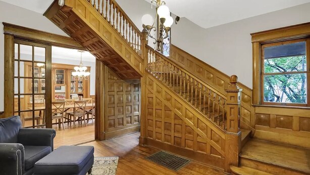 A wooden staircase with a chandelier, a dining area with tables and chairs, and a view through a window. - Woodruff Manor 11 Bedroom Estate - 20+ guests (Indianapolis)