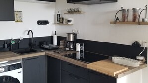 Eine moderne Küche mit schwarzen Schränken, einem Backofen, einer Spüle und einem Herd. Regale mit Gläsern und eine Kaffeemaschine sind ebenfalls vorhanden.