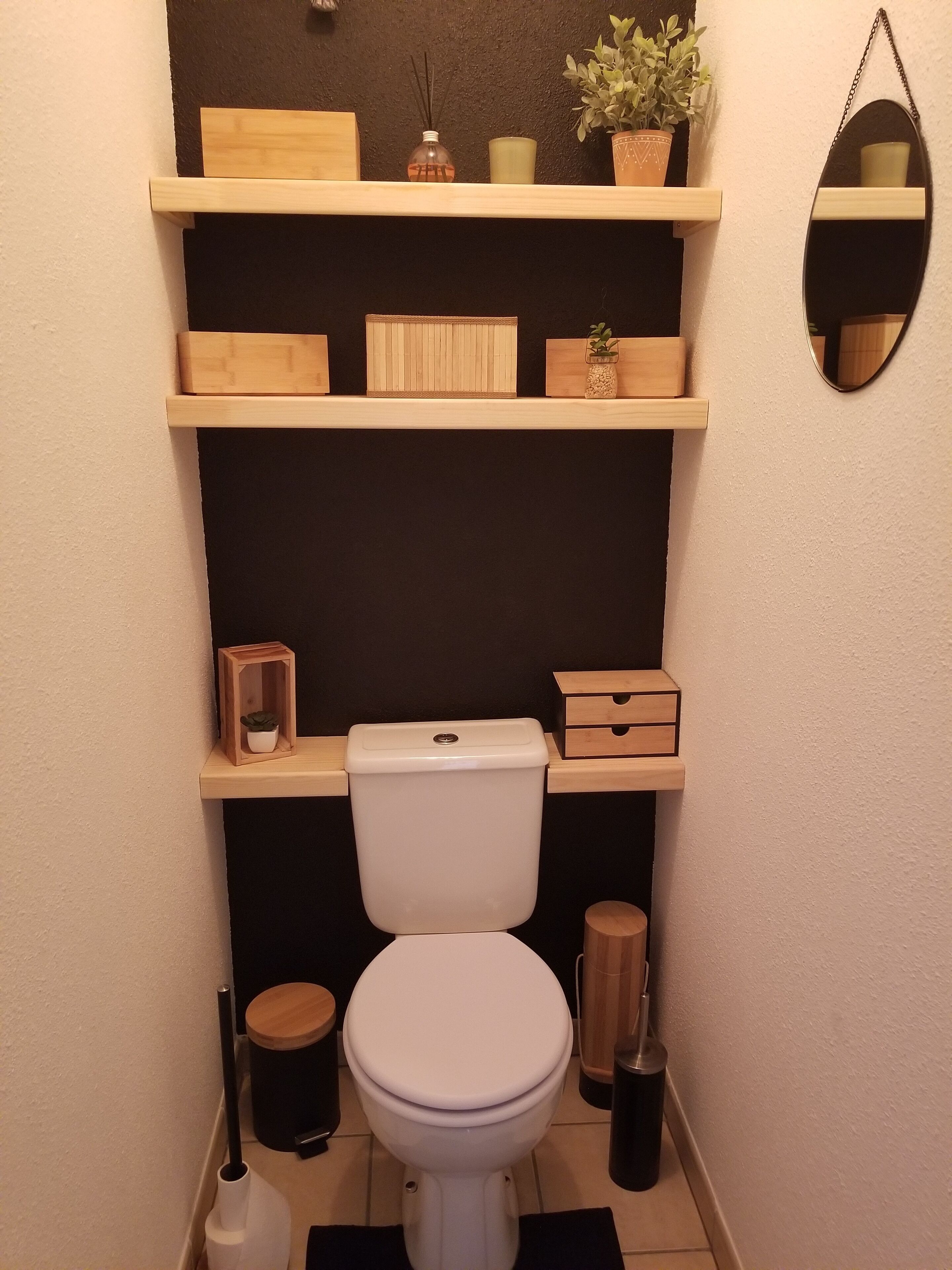 A compact bathroom with a white toilet, wooden shelves above, and a mirror on the wall.
