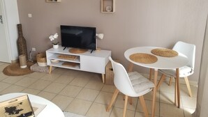 Ein modernes Wohnzimmer mit Fernseher, weißen Stühlen, einem kleinen Esstisch und einem weißen Schrank.