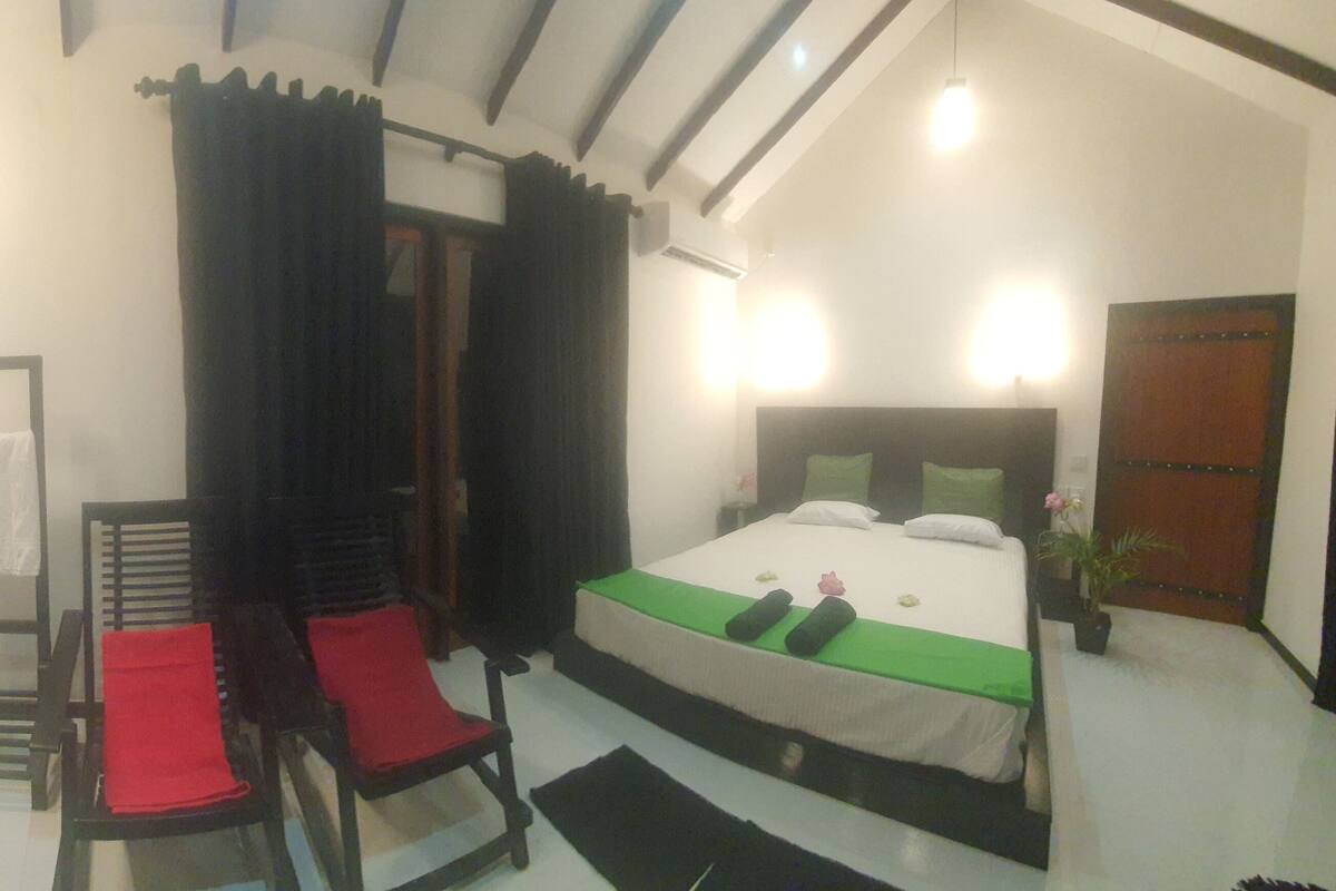 Une chambre à coucher avec un lit, une chaise, une petite table et une fenêtre avec des rideaux.