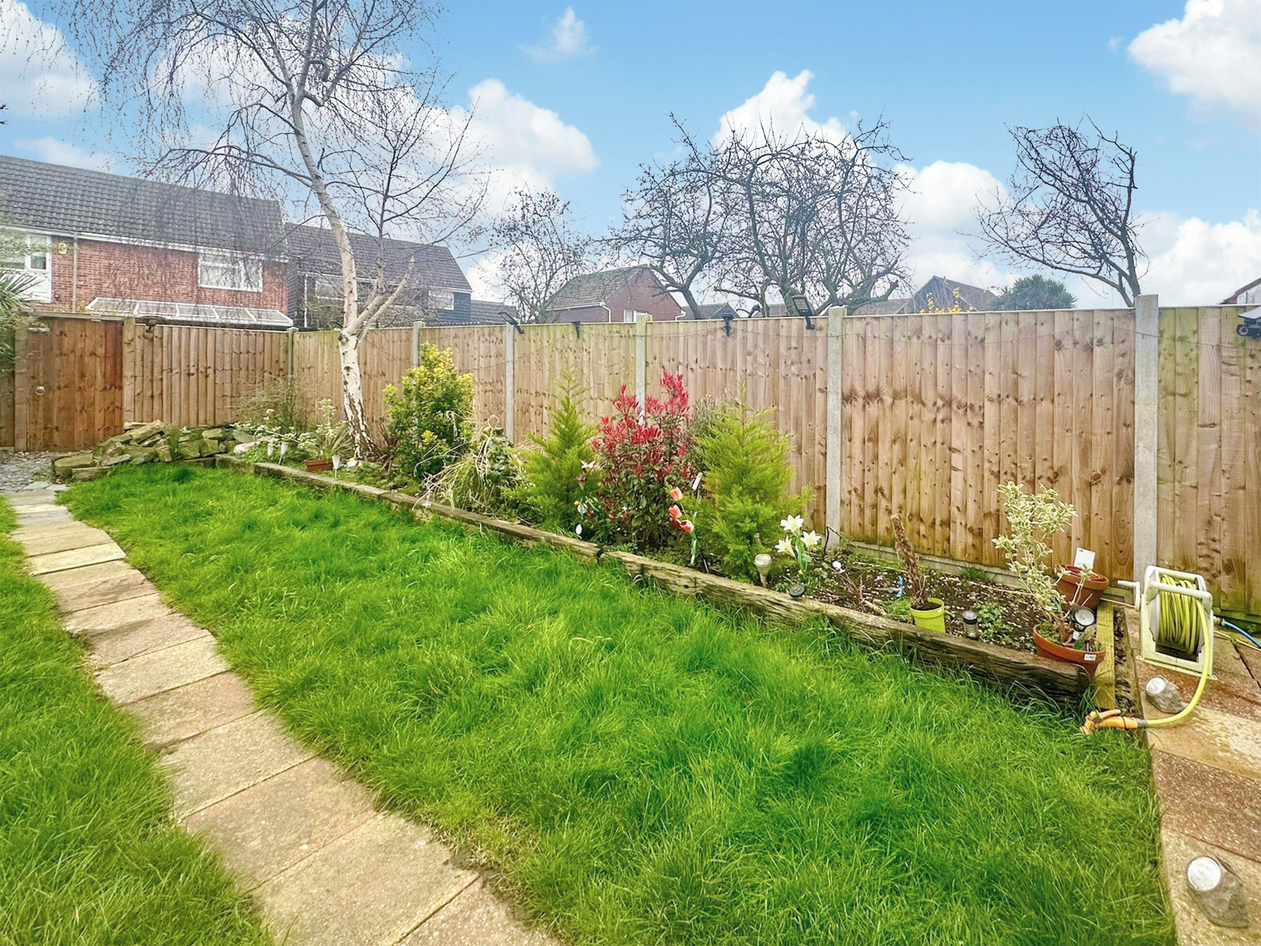 Un jardin avec une clôture en bois, une pelouse verdoyante et diverses plantes en pot.