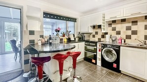 A modern kitchen with a built-in oven, microwave, and washing machine, a bar area with stools, and a large window. - Spacious family house close to beach and amenities. (Clacton on Sea)