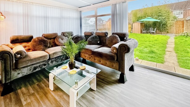 A living room with a glass coffee table, two sofas, and a view of a backyard. - Spacious family house close to beach and amenities. (Clacton on Sea)