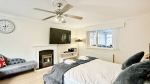 A bedroom with a bed, a sofa, a fireplace, a television, and a window. - Spacious family house close to beach and amenities. (Clacton on Sea)