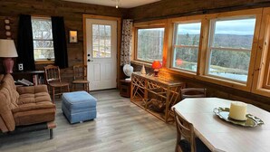 A cozy cabin interior with a wooden floor, a dining table with chairs, a sofa, and a small ottoman. - Magic Forest Farm's Artist Retreat (Coeymans Hollow)