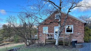 A brick house with a wooden deck, a tree in front, and a trash can. - Magic Forest Farm's Artist Retreat (Coeymans Hollow)