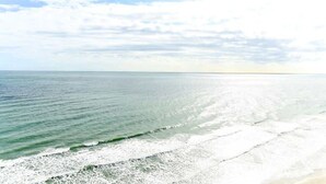Ein Strand mit Wellen, blauem Himmel und weiter Küstenlinie.