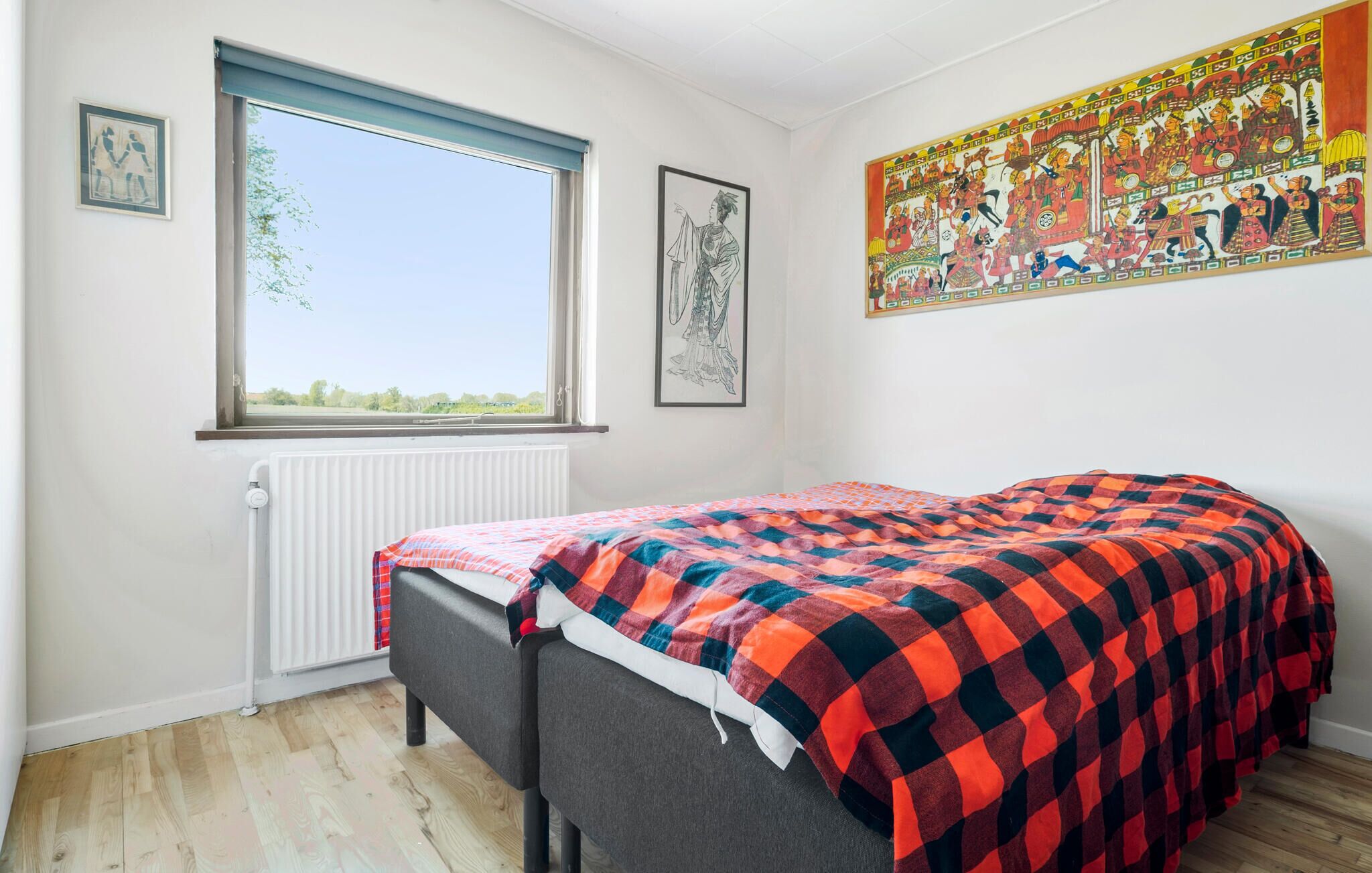 Une chambre à coucher avec un lit, une fenêtre, un radiateur et deux tableaux encadrés accrochés au mur.