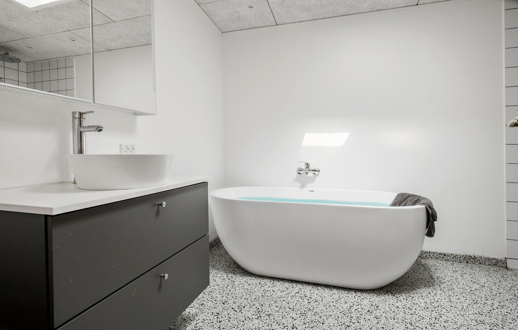 A modern bathroom with a freestanding bathtub, a white sink, and a dark-colored vanity.