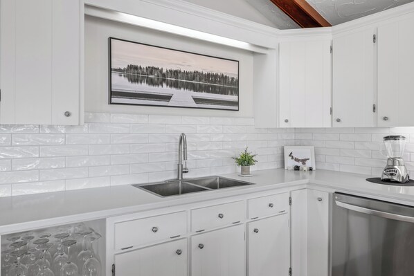 A modern kitchen with white cabinetry, a stainless steel sink, and a blender on the counter.