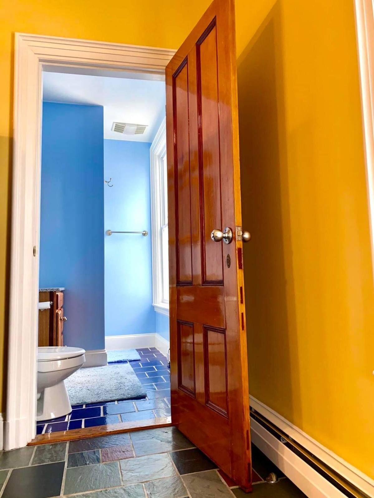 Un pasillo con una puerta de madera que da a un baño con inodoro y pared azul.