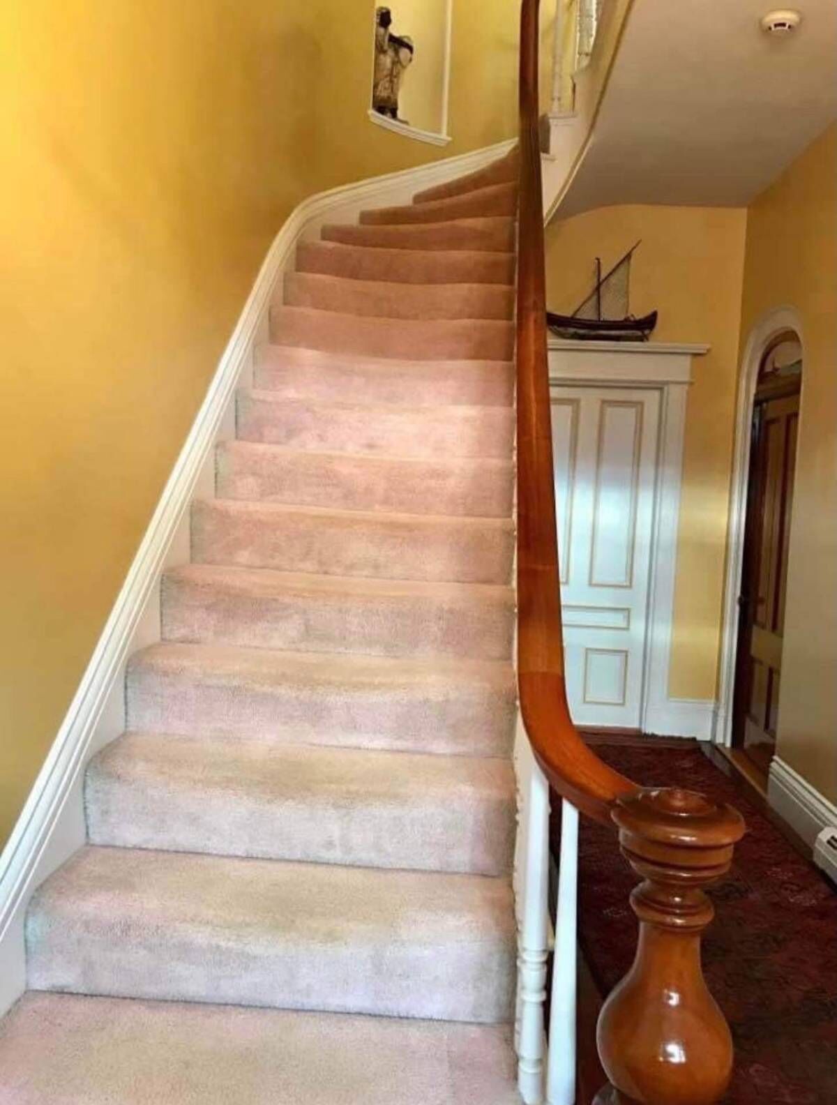 Una escalera con peldaños alfombrados color beige y barandilla de madera.