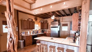 A spacious kitchen with a central island, wooden bar stools, and a rustic tree trunk decoration.