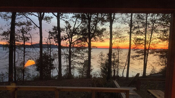 A wooden deck with a railing overlooking a lake at sunset.