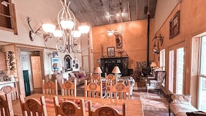 A rustic dining area with a wooden table and chairs, a chandelier, and a stone fireplace.