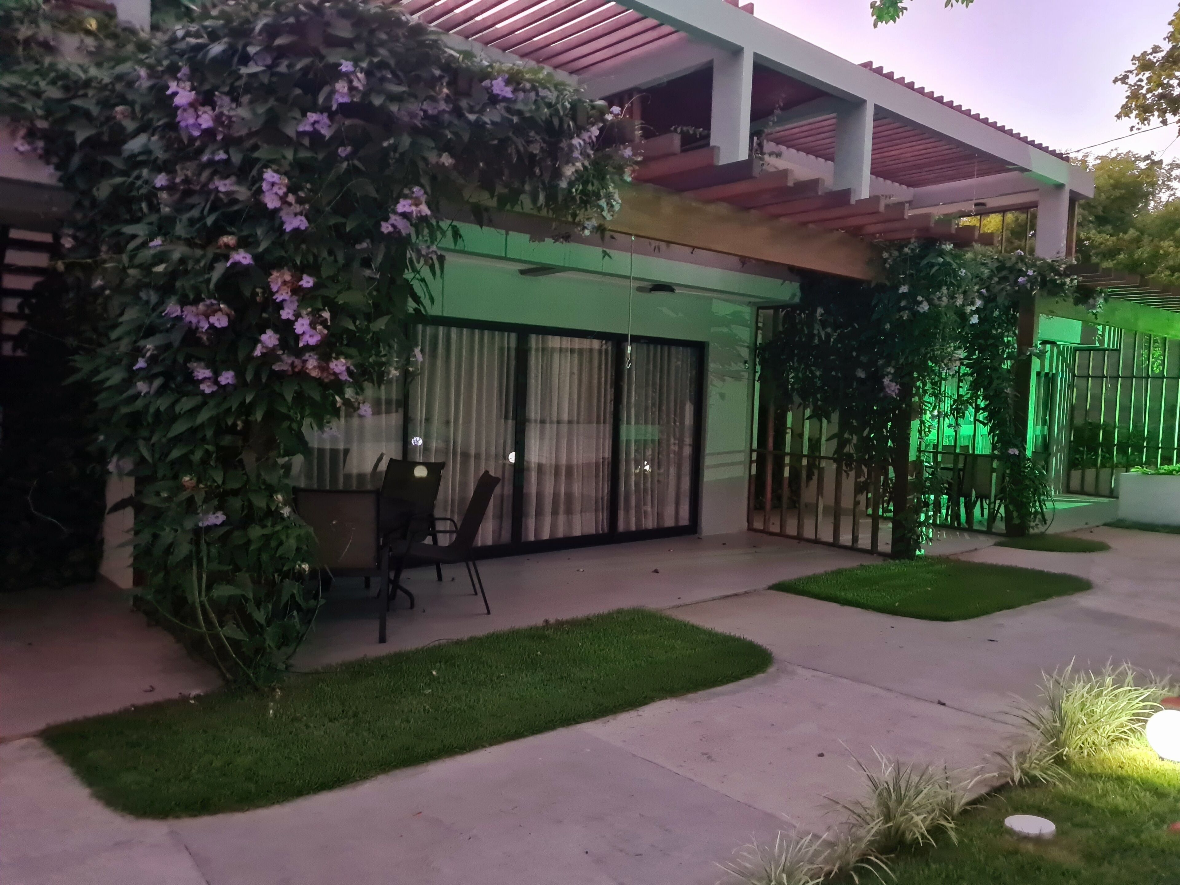 A modern house with a patio area, a covered seating area, and a green-lit fence.
