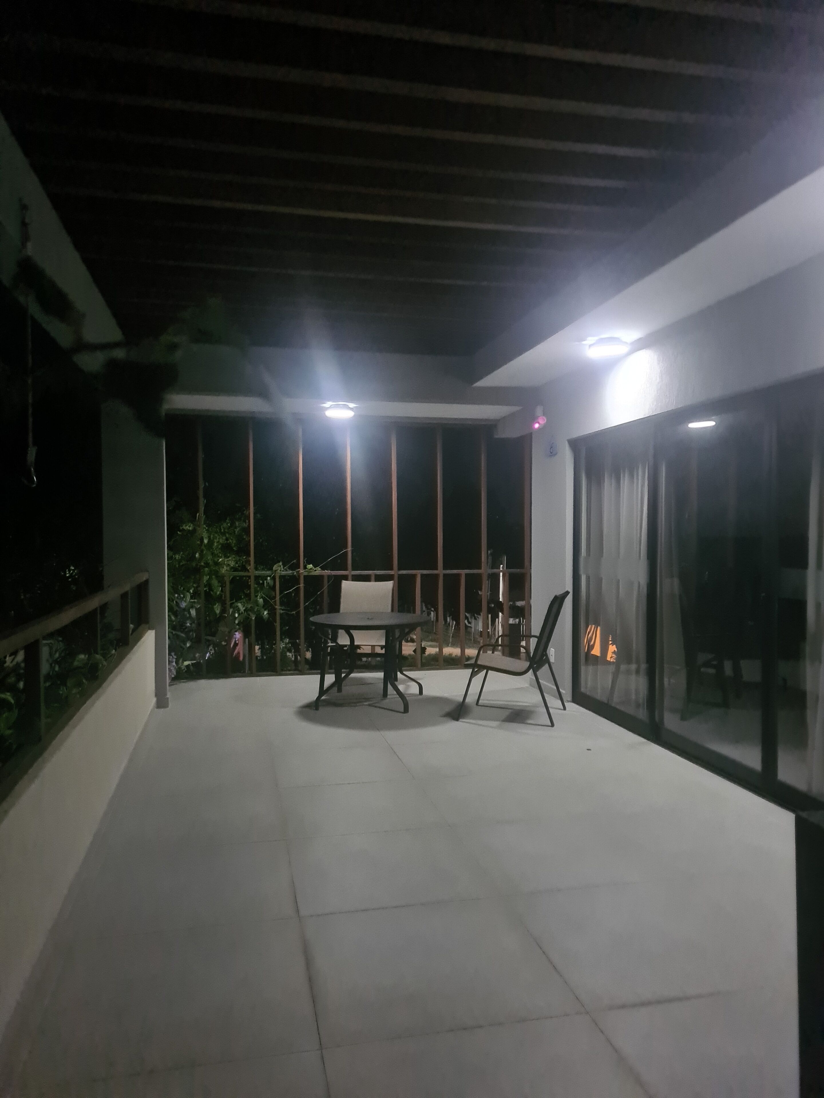 Un patio al aire libre con una mesa, sillas, una puerta de vidrio y una lámpara en el techo.