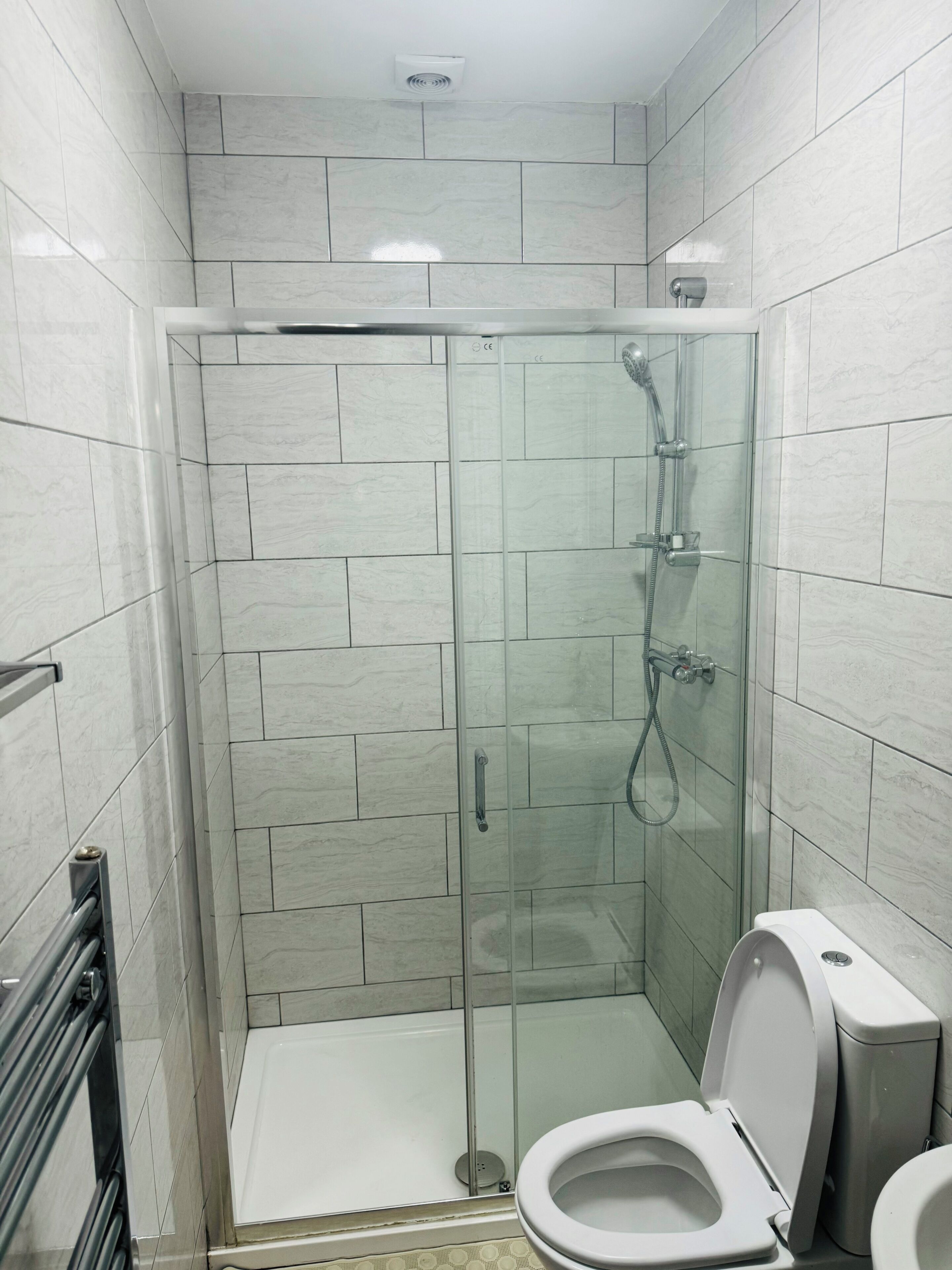 A modern bathroom with a glass-enclosed shower, a toilet, and a hand dryer.