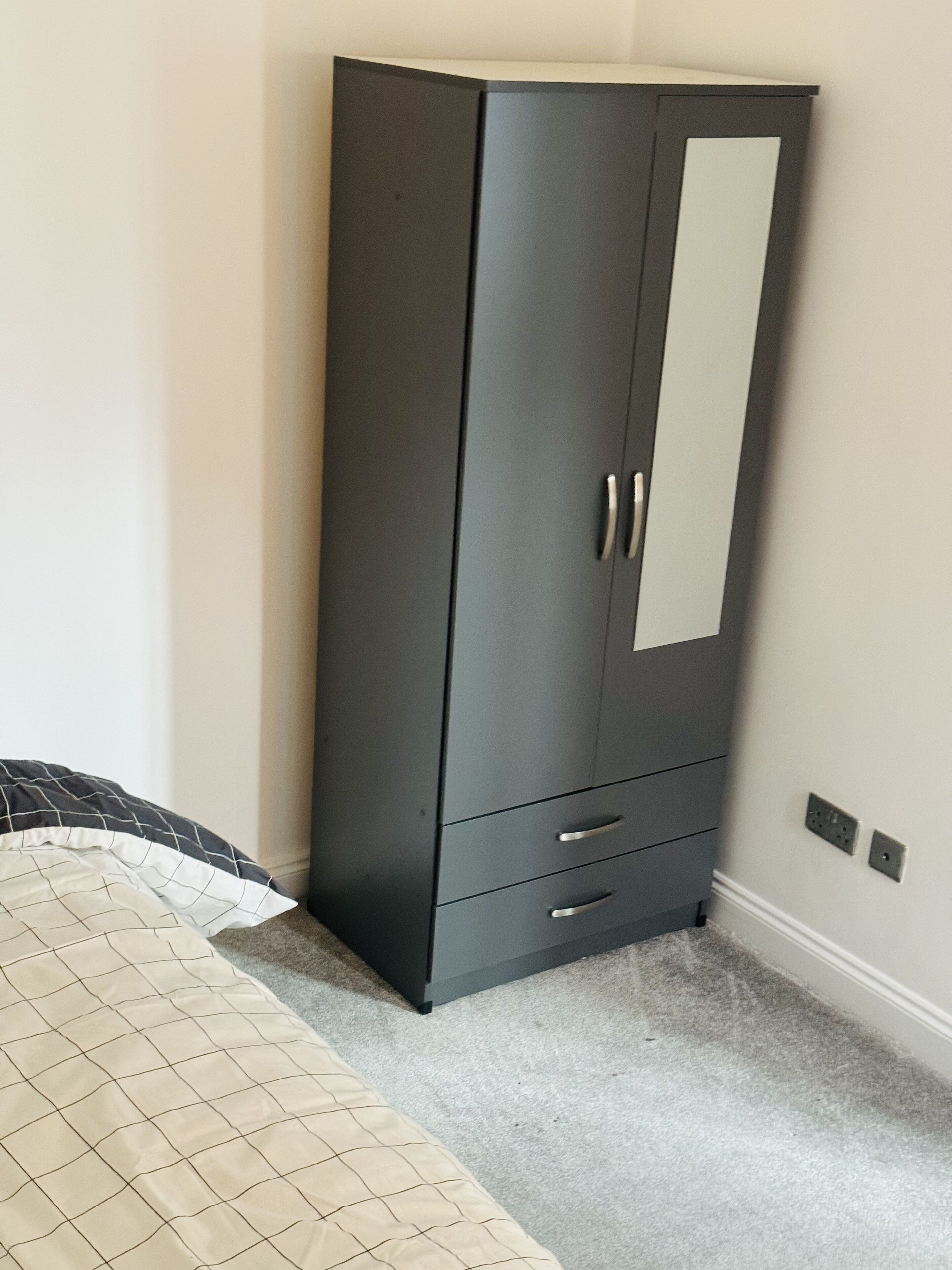 Une grande armoire de couleur sombre, dotée d’une porte miroir et de trois tiroirs.